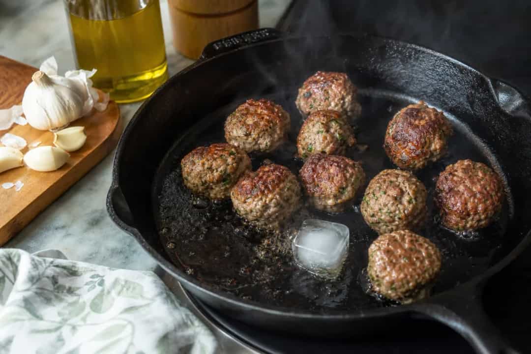 Editorial photo: The Ice-Cube Searing Trick for Juicy Meatballs (tips tricks tip) — realistic home-kitchen scene with visible tools and ingredients in natural l