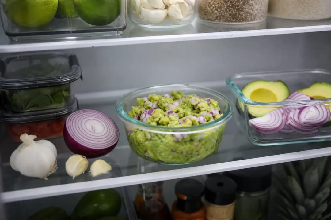 Halved avocados with lemon and plastic wrap on a cutting board to slow browning