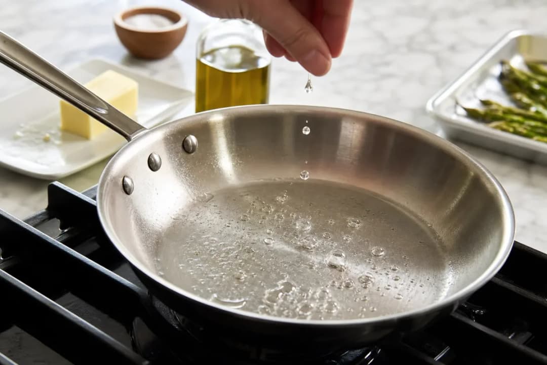 Editorial photo: How to Prevent Food from Sticking: The Water Drop Test (pro techniques tip) — realistic home-kitchen scene with visible tools and ingredients i