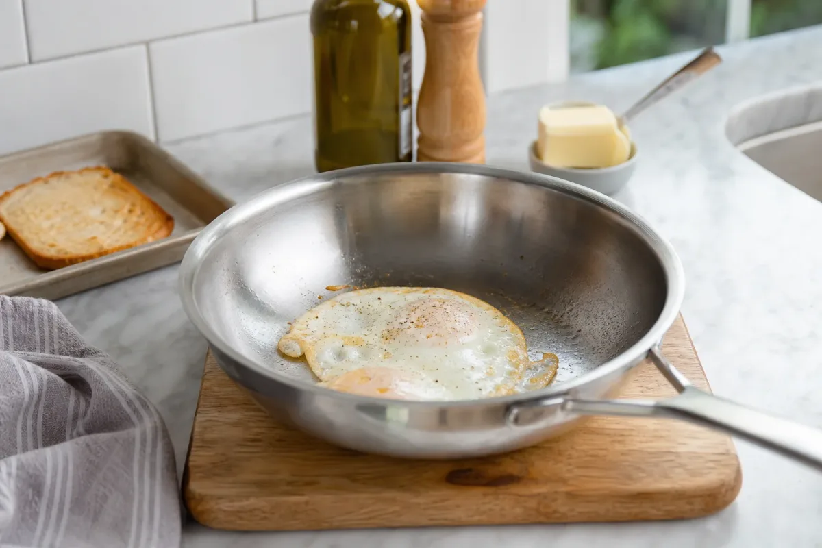 Editorial photo: How to Stop Eggs from Sticking to Stainless Steel Pans (quick fixes tip) — realistic home-kitchen scene with visible tools and ingredients in n