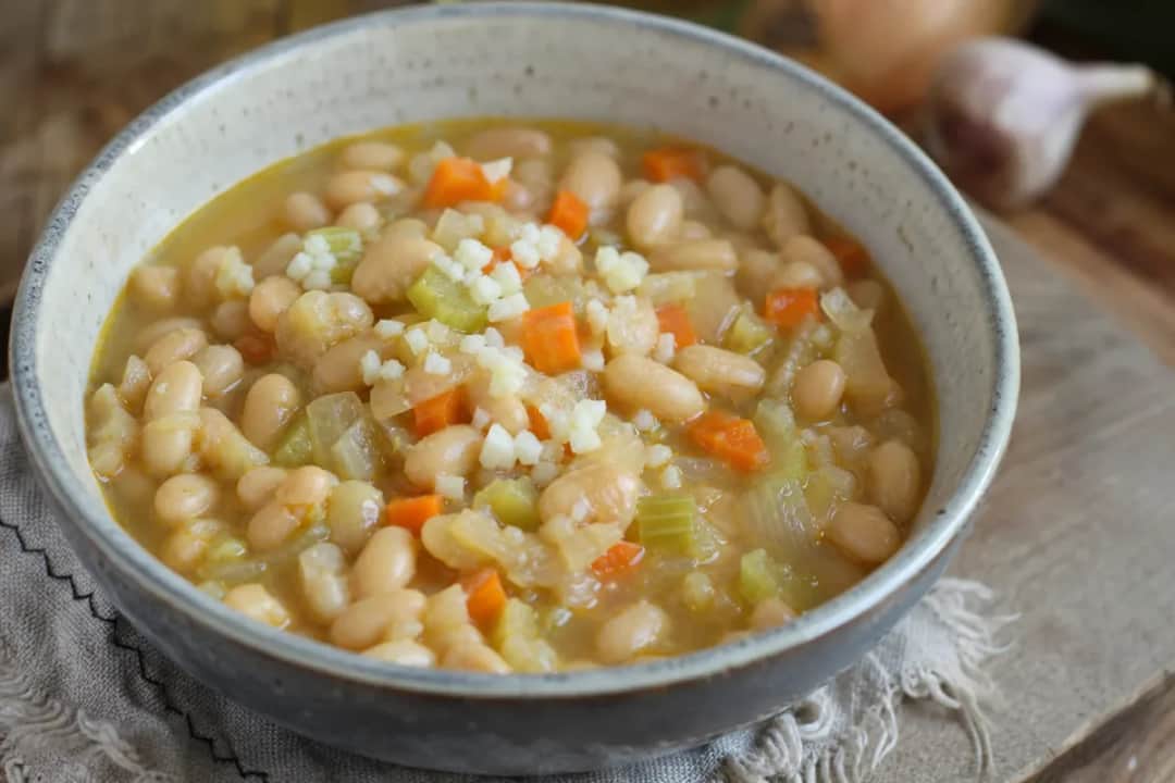Thick white bean stew with vegetables, garnished with parsley in a bowl.