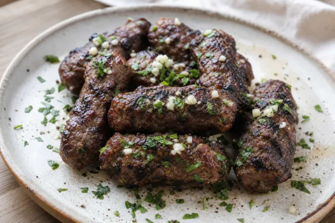 Grilled Albanian qofte served on a plate, garnished with fresh herbs and a side of vegetables.