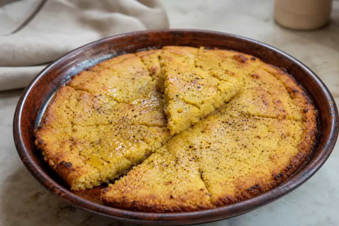 Golden-brown chickpea pie topped with cumin and served in slices, garnished with herbs.