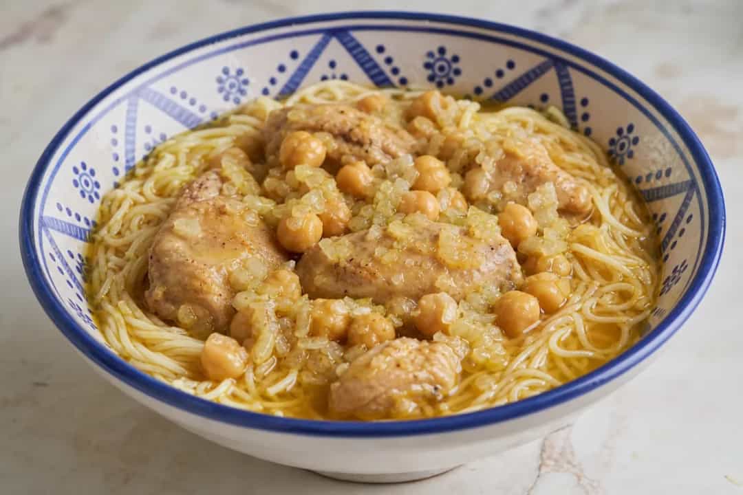 Plate of Algerian Rechta noodles with chicken, chickpeas, and herbs garnished with spices.