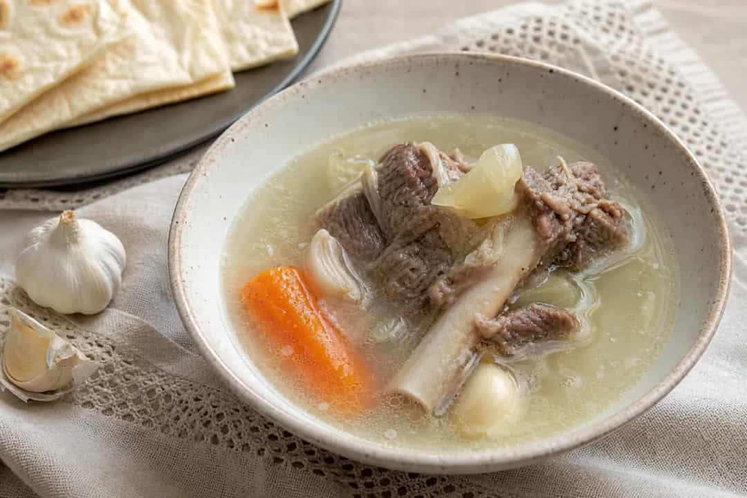 A warm bowl of Armenian Khash soup with tender meat, garlic, and crispy lavash bread.