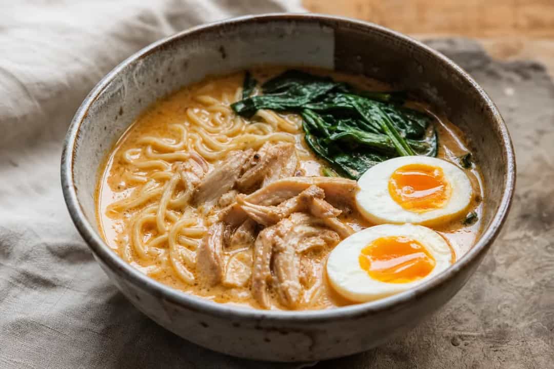 Bowl of ramen topped with soft-boiled eggs, vibrant curry broth, and fresh herbs.