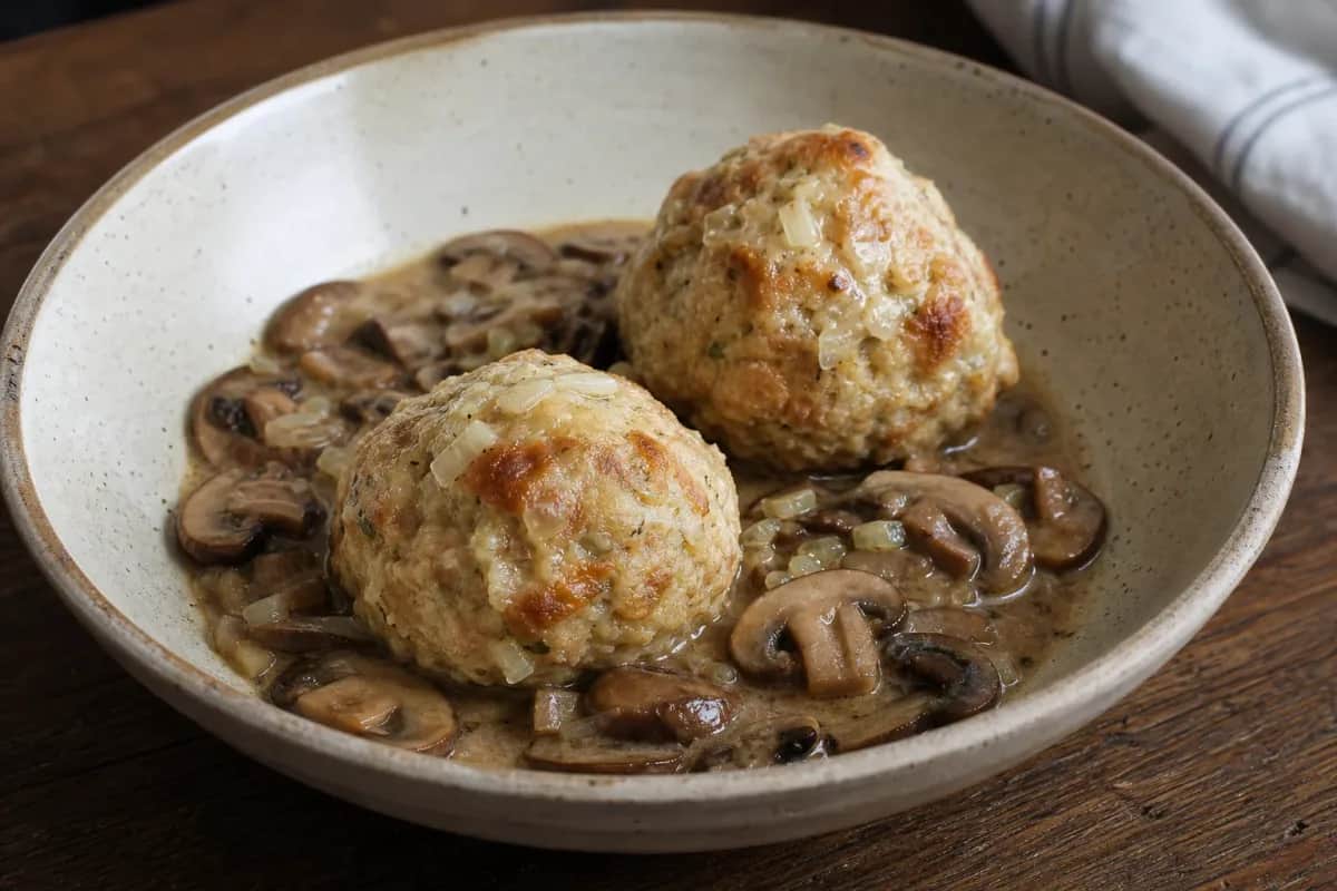 Fluffy bread dumplings topped with creamy mushroom sauce and fresh parsley on a white plate.