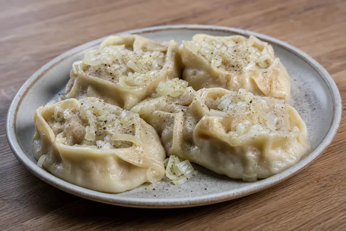 Steamed Kazakh Manty dumplings served with a sprinkle of herbs and spices, showcasing their soft, fluffy texture.