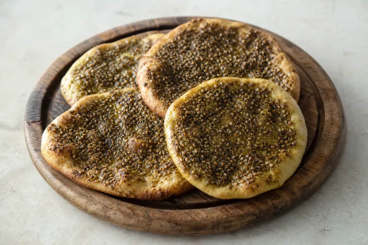 Golden brown manakish topped with za’atar and olive oil, served on a wooden board.