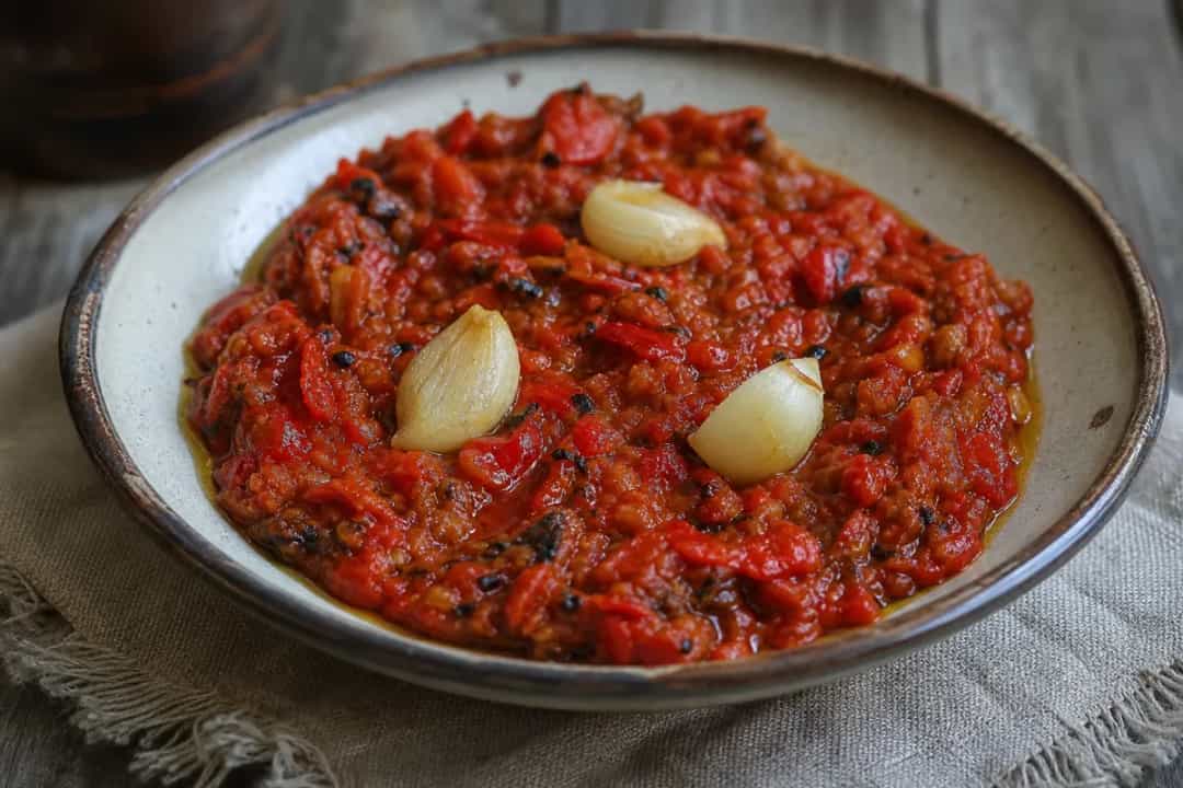 Smooth, vibrant ajvar spread in a bowl, garnished with herbs and served with crusty bread.