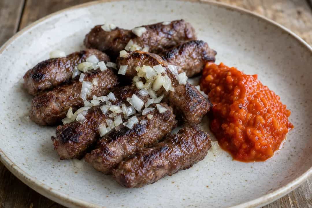 Plated Serbian ćevapi with grilled onions, ajvar, and fresh bread, showcasing the juicy texture.
