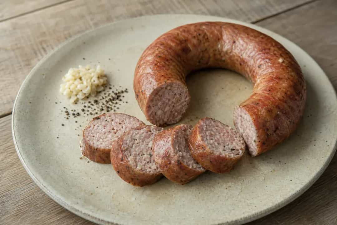 Sliced Carniolan sausage on a wooden board, garnished with parsley and mustard.