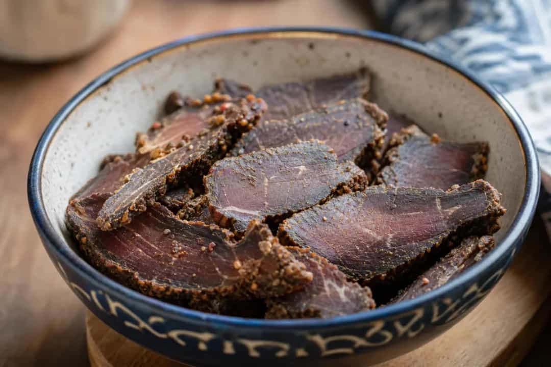 Slices of beef biltong with a spiced crust on a wooden board
