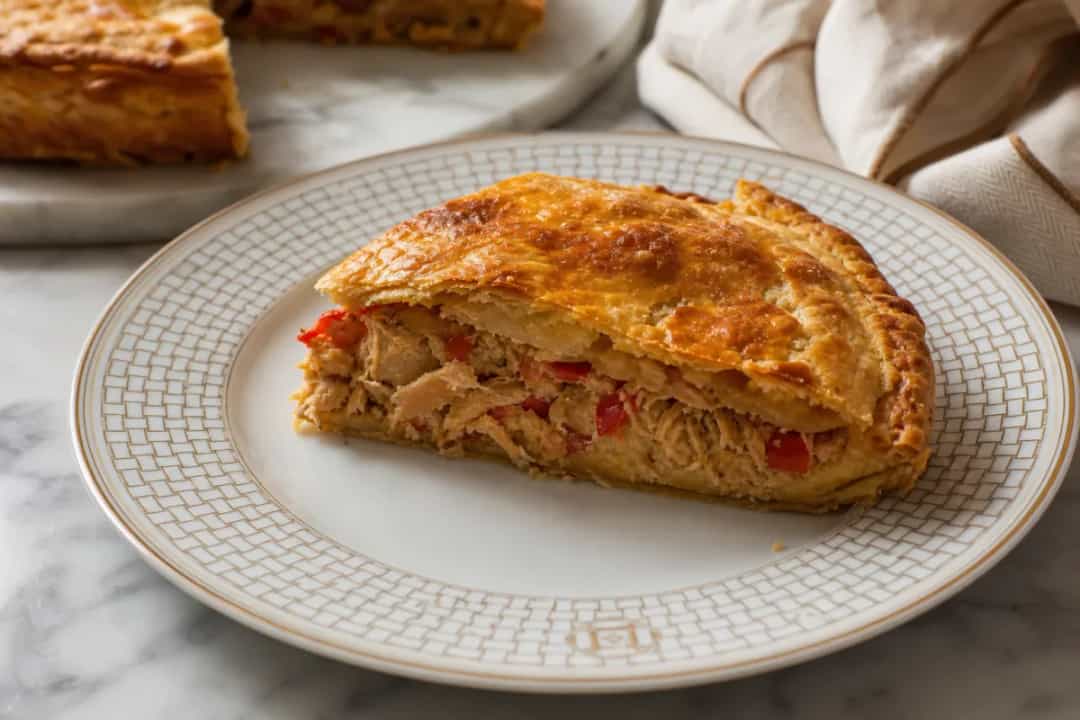 Golden Spanish empanada gallega filled with tuna and bell peppers, served warm on a plate.