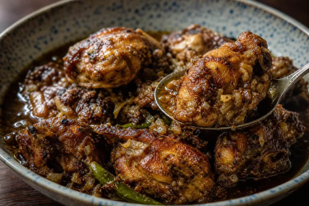 A bowl of Sri Lankan chicken curry with rich spices, garnished with fresh herbs and served with rice.