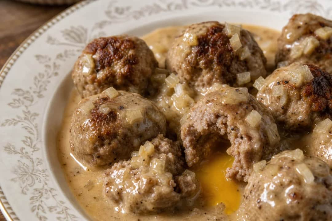 Plated Swedish meatballs with rich creamy gravy, garnished with parsley and served with lingonberry jam.