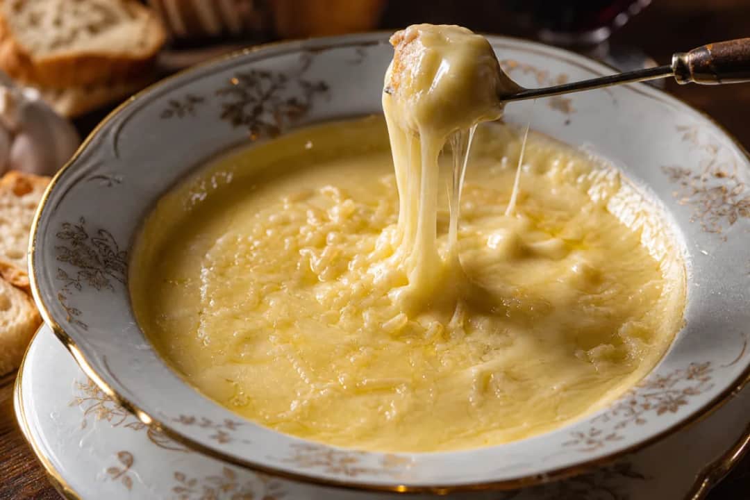 A pot of creamy Swiss cheese fondue with bread cubes for dipping, garnished with herbs.