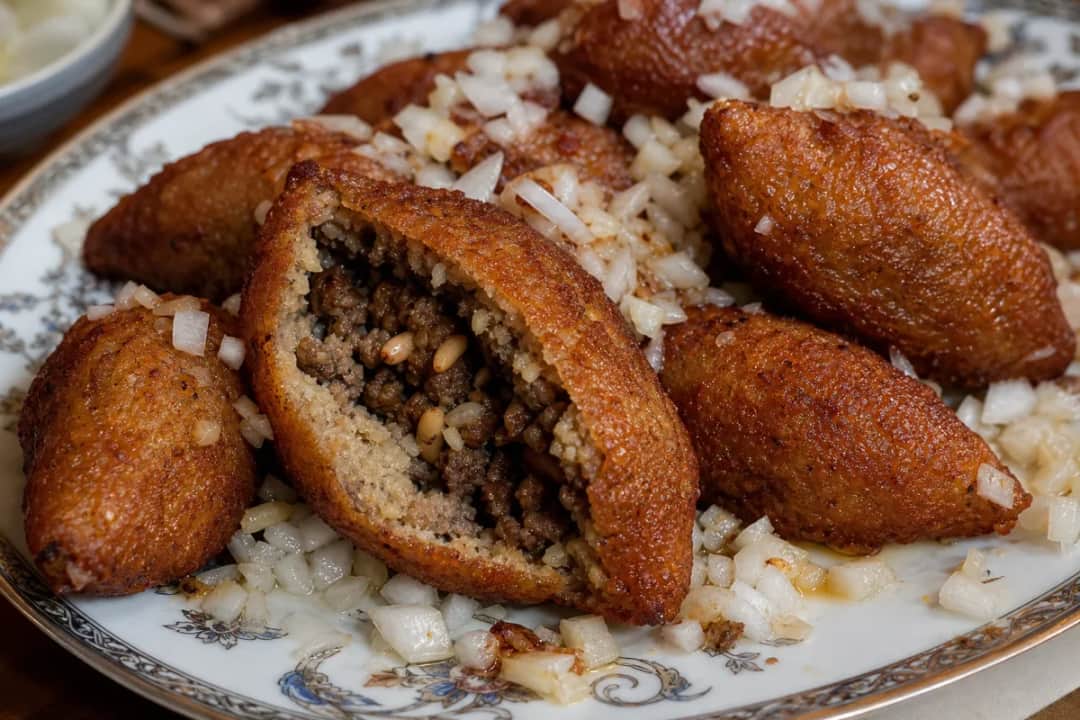 Plated Syrian kibbeh featuring crispy bulghur shells filled with spiced meat and pine nuts.