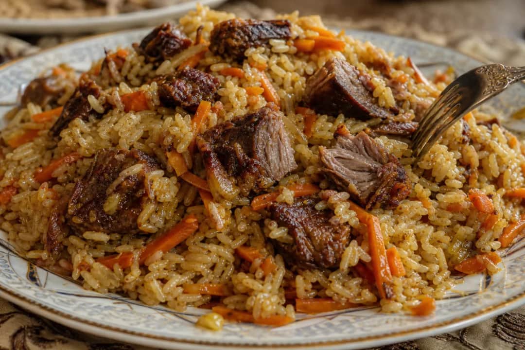 A bowl of Uzbek plov featuring tender beef, colorful carrots, and fluffy rice, garnished with fresh herbs.