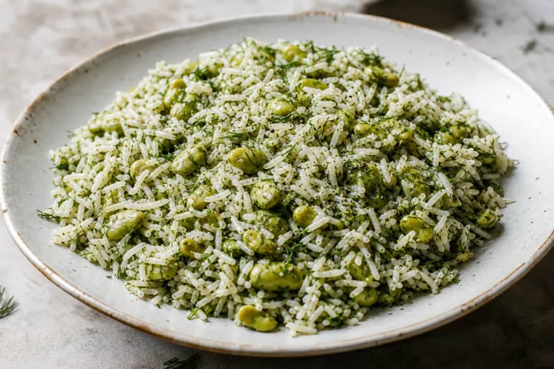 Fluffy saffron rice garnished with fresh dill and fava beans, served elegantly.