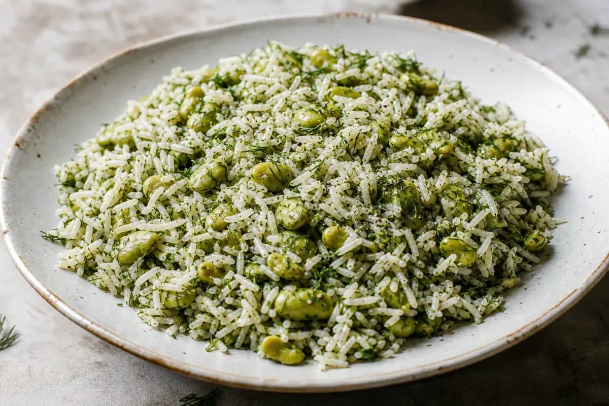 Fluffy saffron rice garnished with fresh dill and fava beans, served elegantly.