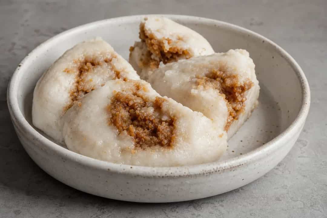 Steamed rice cakes with a golden layer of coconut and date molasses, served on a leaf.