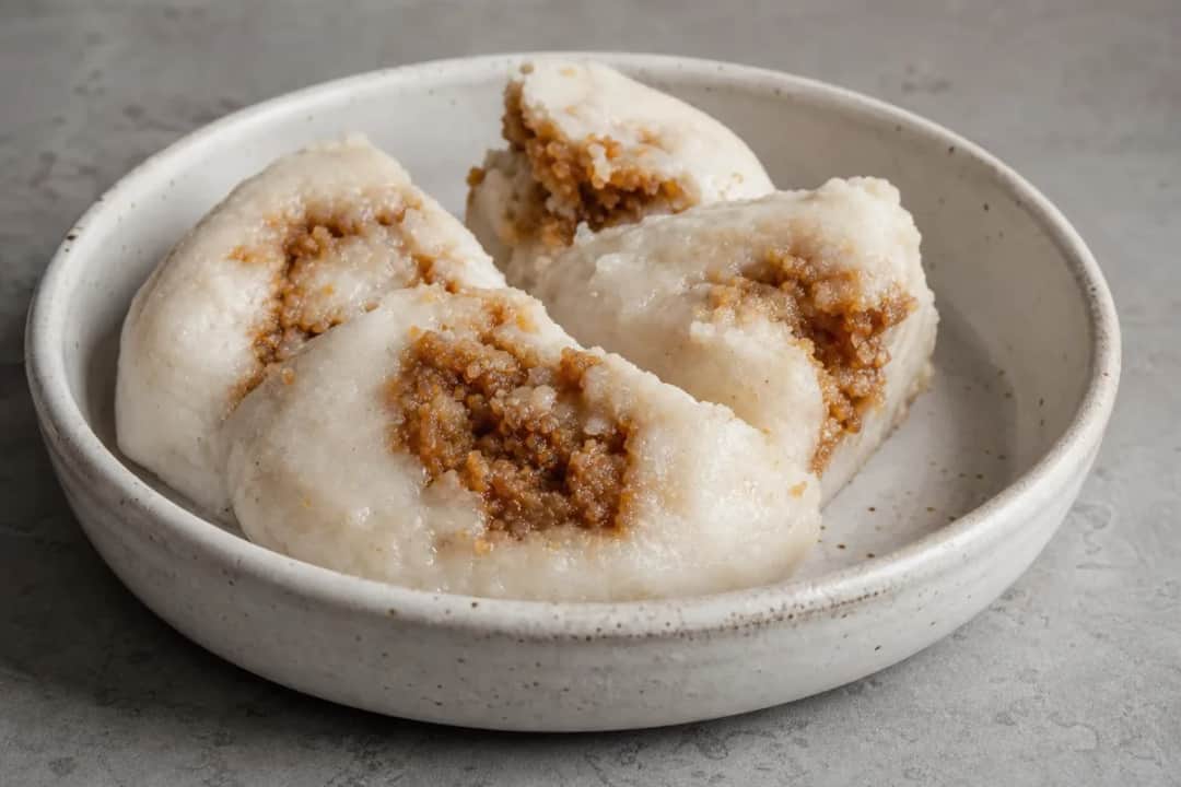 Steamed rice cakes with a golden layer of coconut and date molasses, served on a leaf.