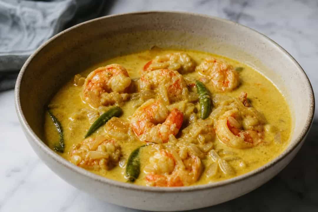 Creamy Chingri Malai Curry with prawns, coconut milk, and spices garnished with cilantro on a white plate.