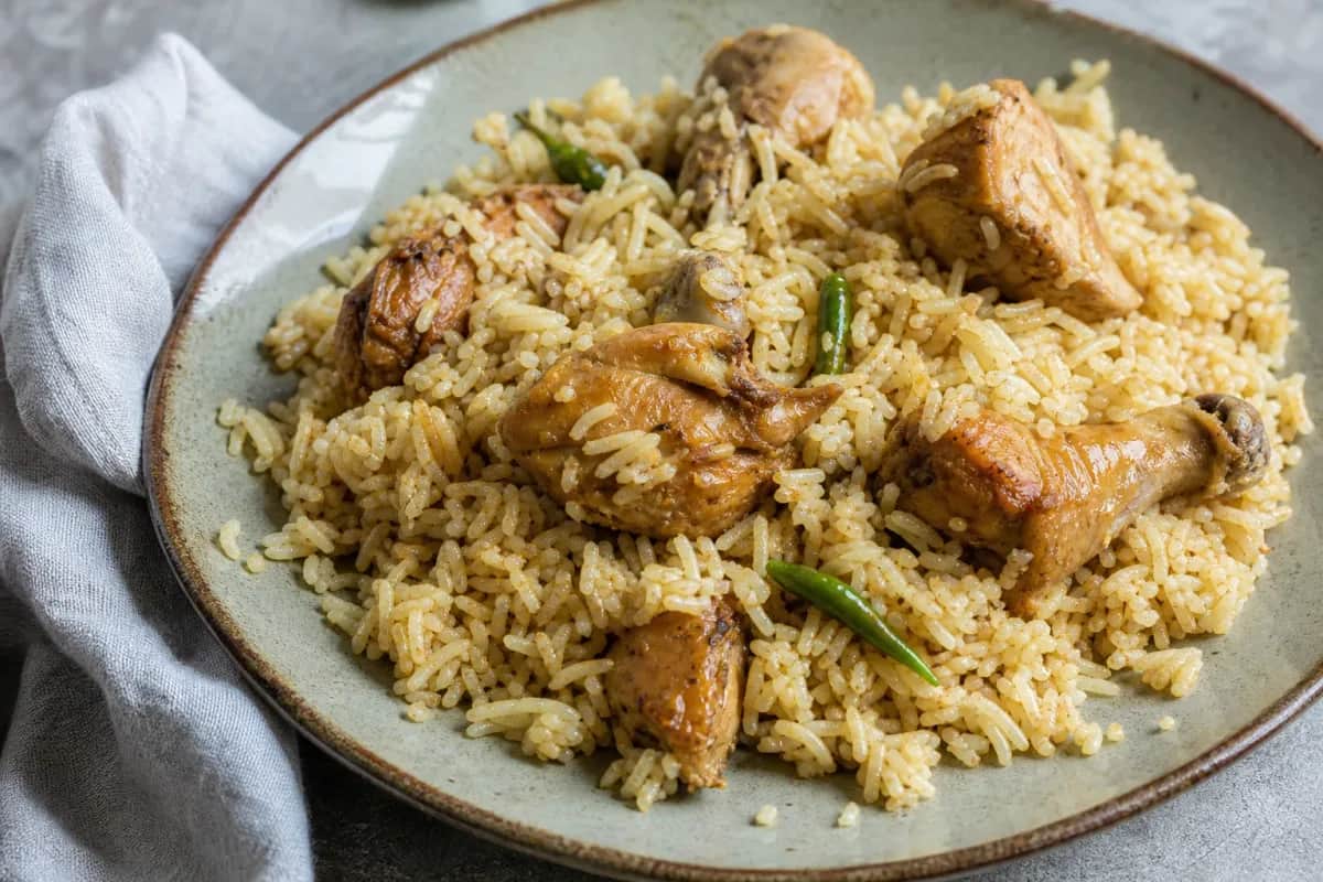 A vibrant plate of Morog Polao featuring tender chicken pieces atop fluffy fragrant rice garnished with fresh herbs.
