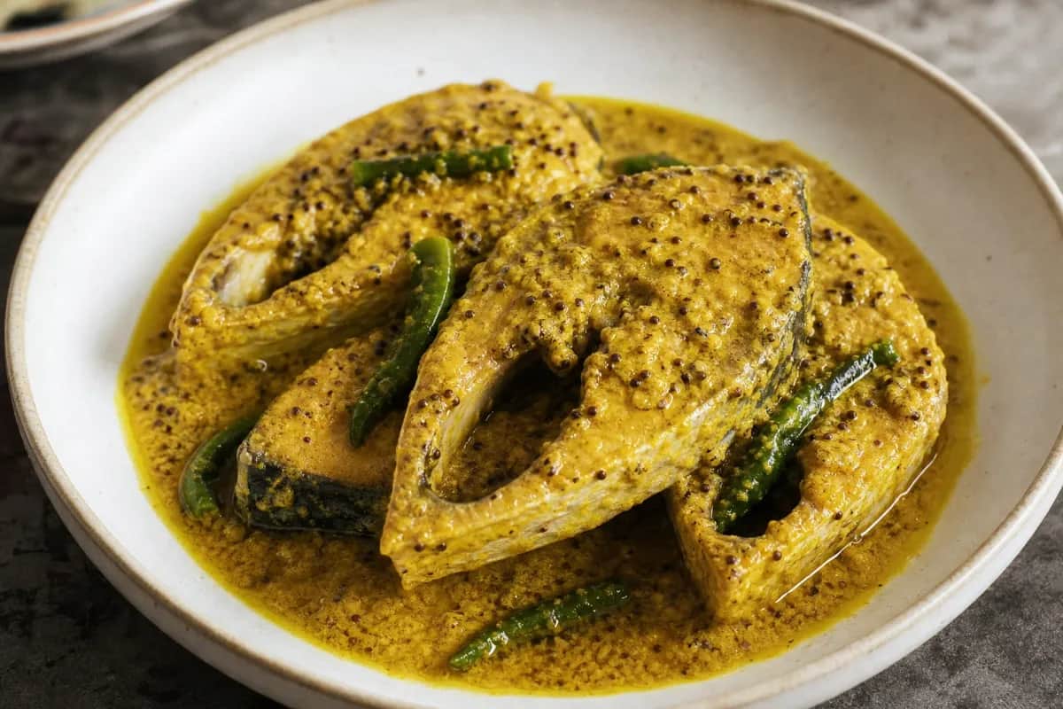 Plated Hilsa fish in a creamy mustard sauce, garnished with green chilies and served with rice.