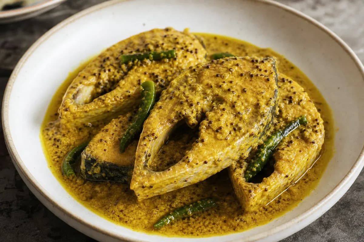 Plated Hilsa fish in a creamy mustard sauce, garnished with green chilies and served with rice.