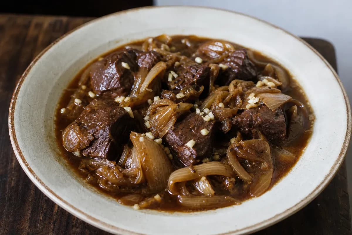 A hearty bowl of beef carbonnade with dark beer, tender beef pieces, and caramelized onions garnished with fresh herbs.