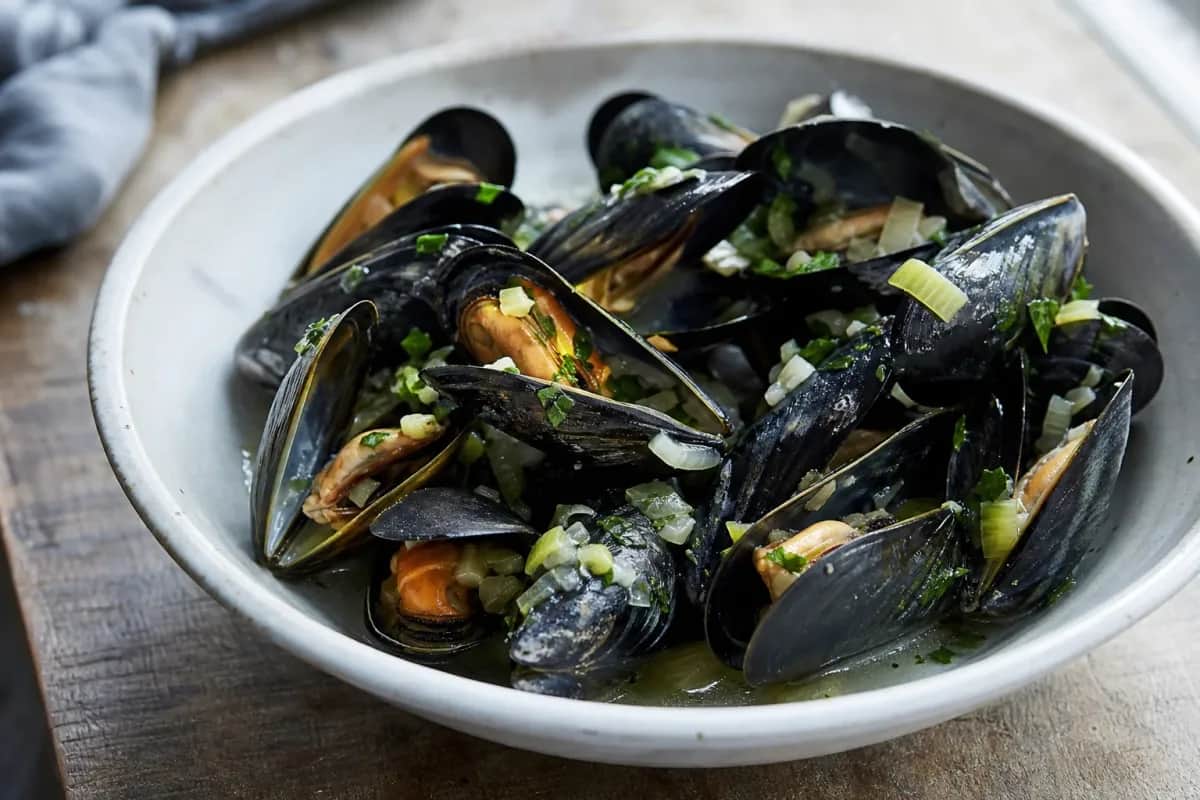 Plated moules-frites featuring plump mussels, golden fries, and fresh herbs garnishing the dish.