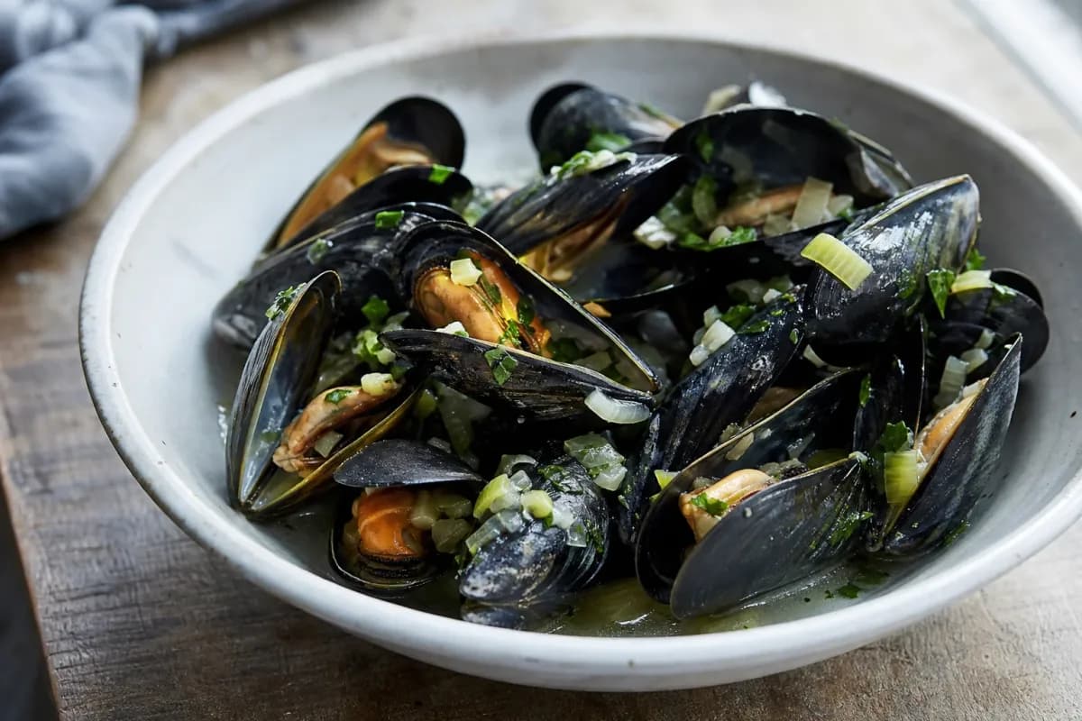 Plated moules-frites featuring plump mussels, golden fries, and fresh herbs garnishing the dish.