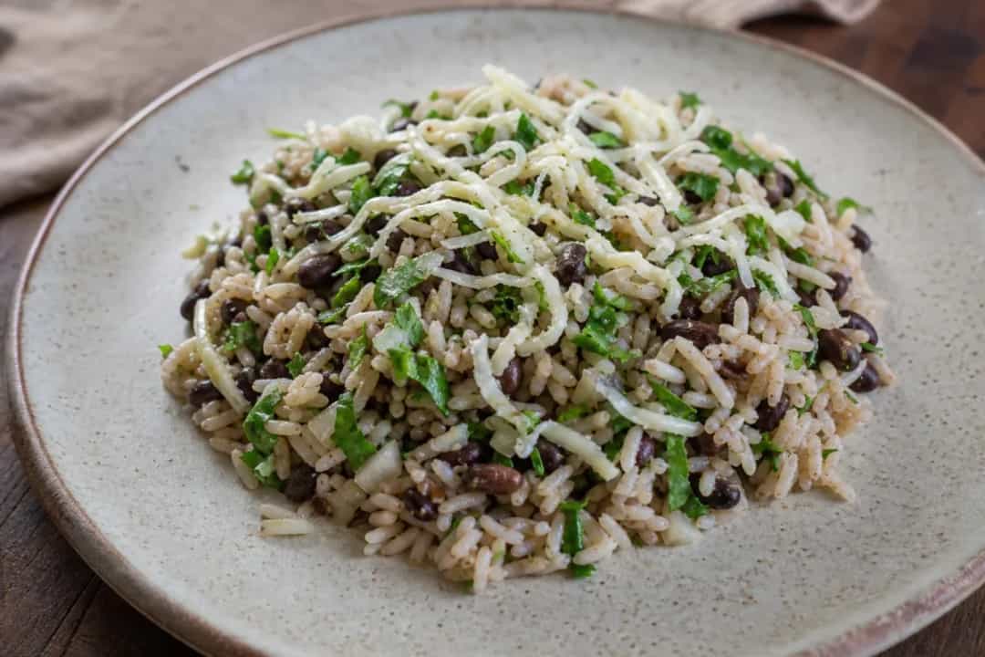 A colorful plate of Baião de Dois featuring fluffy rice, black beans, and melted cheese garnished with fresh herbs.