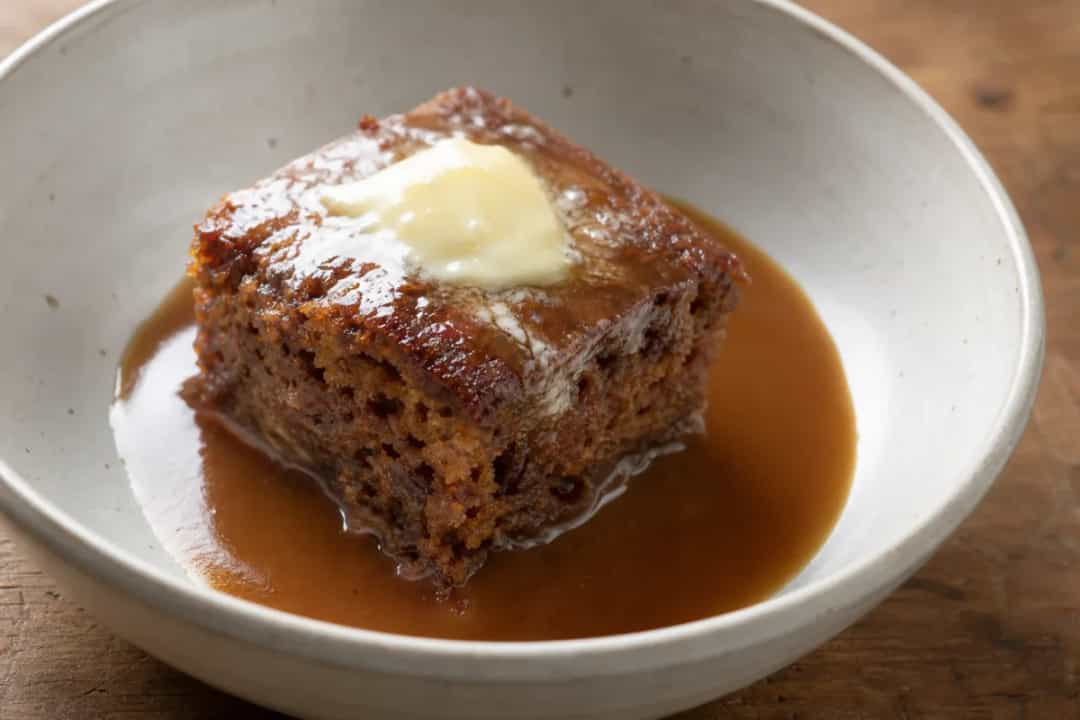Rich sticky toffee pudding topped with warm caramel sauce and a scoop of vanilla ice cream.
