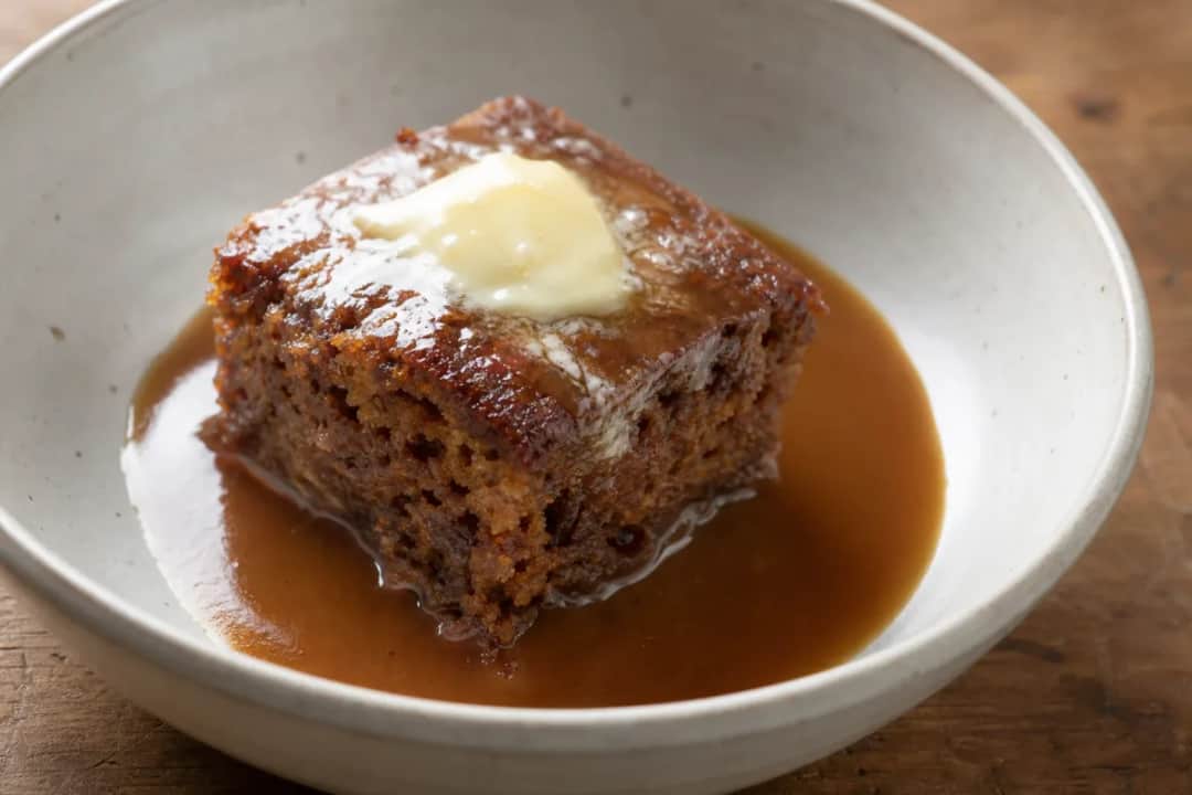 Rich sticky toffee pudding topped with warm caramel sauce and a scoop of vanilla ice cream.