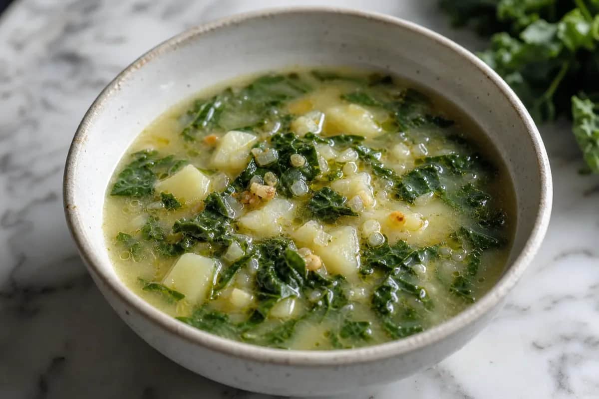 A bowl of Caldo Verde soup with vibrant green kale, creamy potatoes, and a drizzle of olive oil, garnished with slices of chorizo.