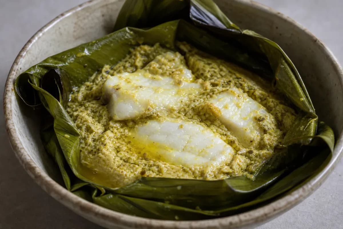 Steamed fish amok served in banana leaves, garnished with herbs and coconut milk.