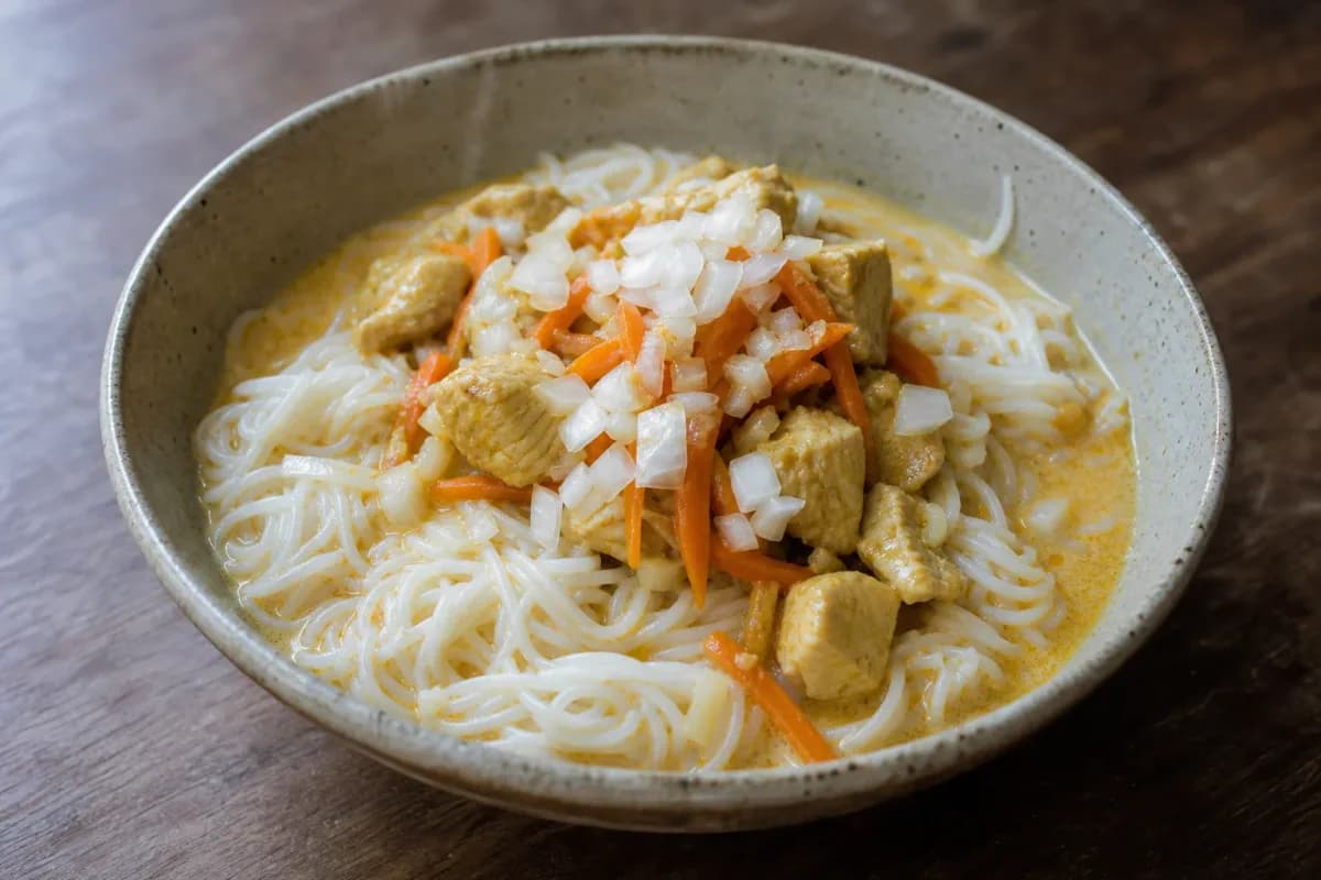 Bowl of Nom Banh Chok with vibrant curry sauce, fresh herbs, and colorful vegetables.
