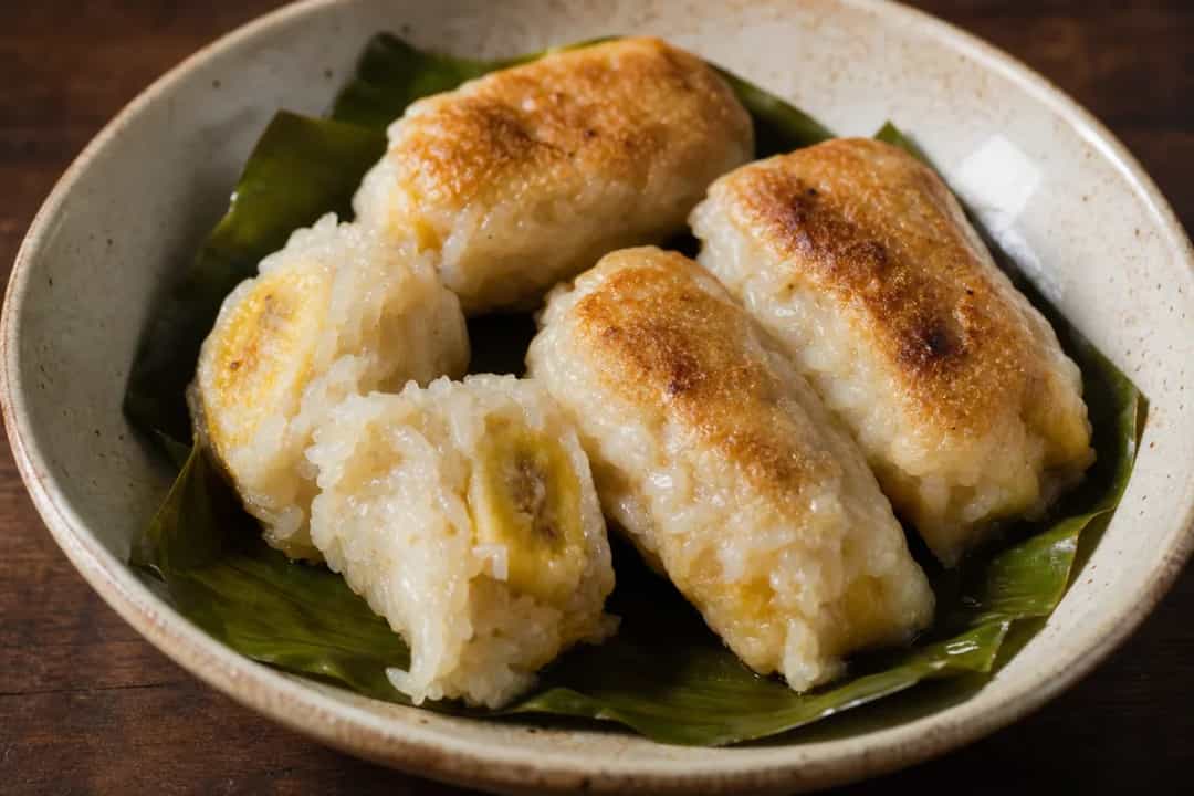 Steamed banana cakes showing sticky rice, banana slices, and coconut filling, wrapped in green banana leaves.
