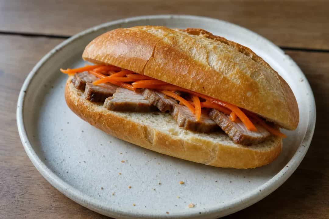 A sliced Num Pang sandwich featuring marinated pork, fresh cilantro, and colorful pickled vegetables on a crusty baguette.