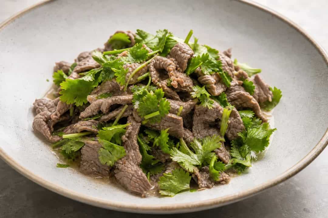 A vibrant Cambodian beef salad topped with fresh herbs and lime, showcasing colorful textures and ingredients.
