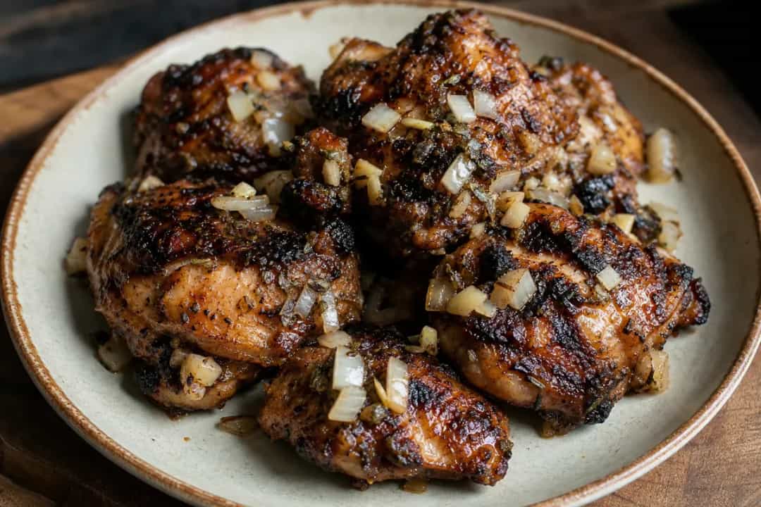 Grilled jerk chicken served with fresh herbs, showcasing its spicy marinade and crispy skin.