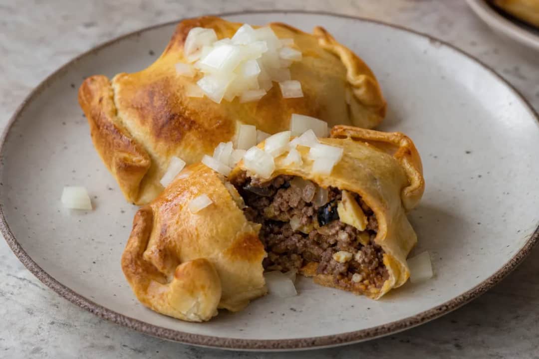 Golden-brown empanadas filled with beef, onions, and olives, arranged on a plate.