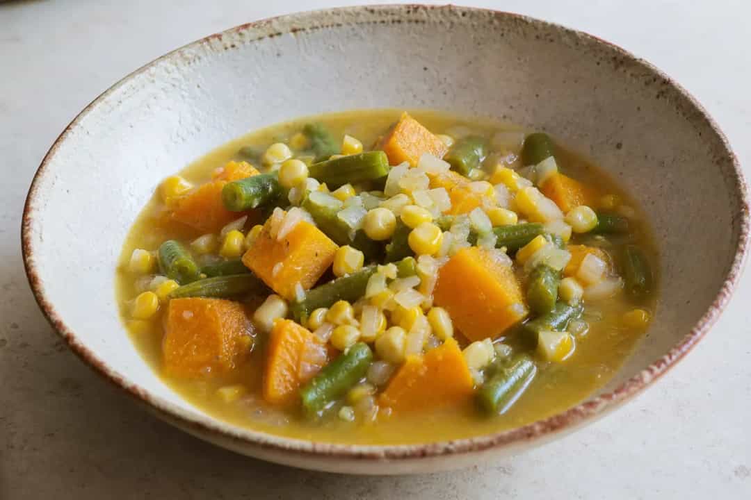 A vibrant bowl of porotos granados featuring colorful beans, sweet corn, and tender pumpkin, garnished with fresh herbs.