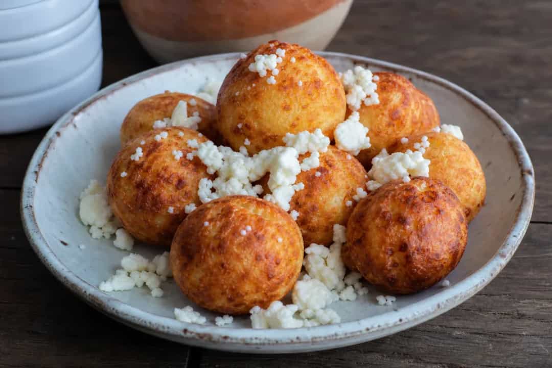 Golden-brown buñuelos with a crispy texture and cheese filling, served on a plate.