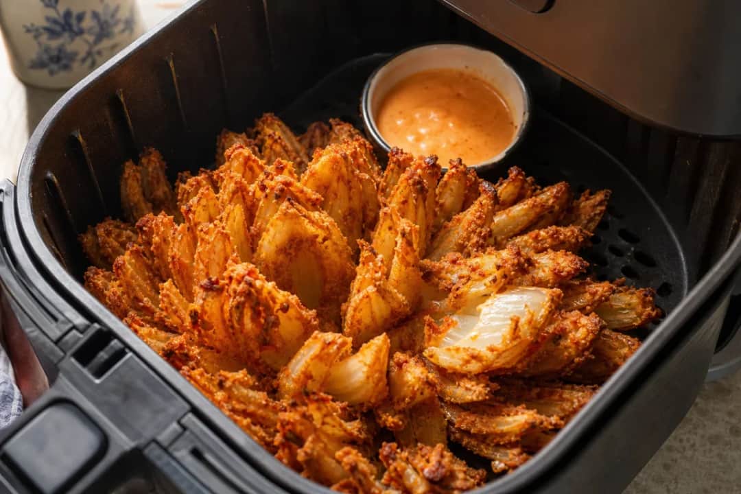 Crispy blooming onion with golden petals served with spicy dipping sauce.