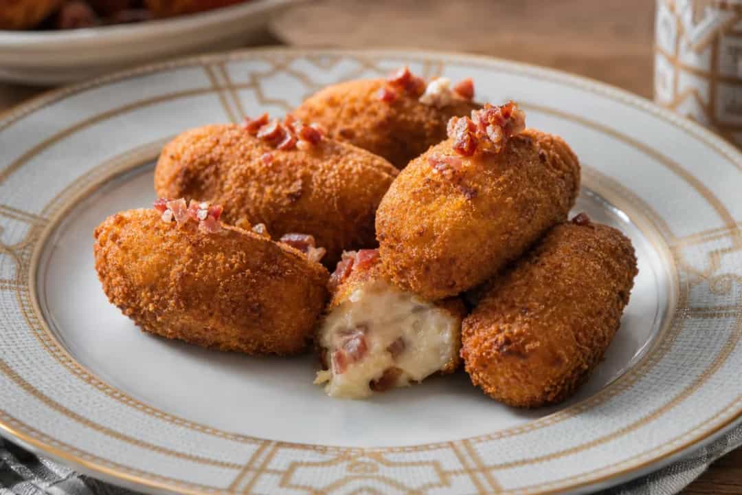 Golden brown Spanish ham croquettes with a crispy exterior and creamy filling, served on a white plate.