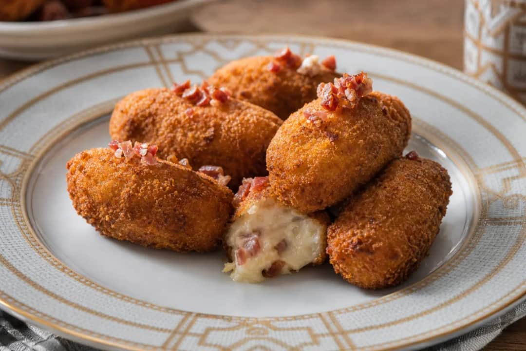 Golden brown Spanish ham croquettes with a crispy exterior and creamy filling, served on a white plate.